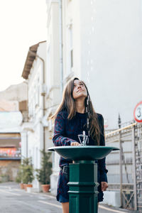 Beautiful woman standing by drinking fountain against building