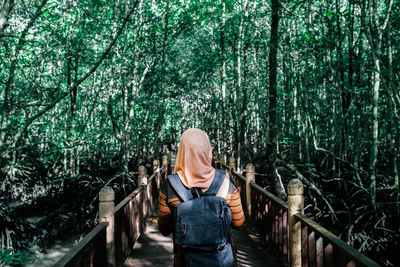 Rear view of woman standing on footbridge in forest