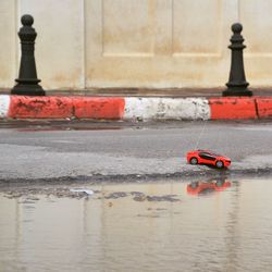 Red toy car on street by puddle
