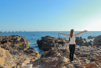 Rear view of woman standing on rocks against sea and clear sky