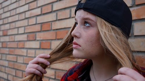 Young woman holding her long blond hair by brick wall