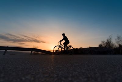 Woman riding bicycle on road against sky during sunset