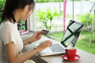 Young woman holding credit card while using laptop at home