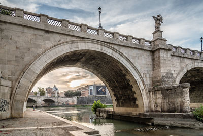 Arch bridge over river against cloudy sky