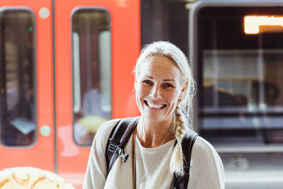 Portrait of smiling mature woman with backpack standing at train station