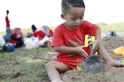 Cute boy playing with shovel while sitting on field