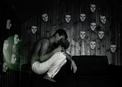 Side view of shirtless man holding flowers while sitting on sofa