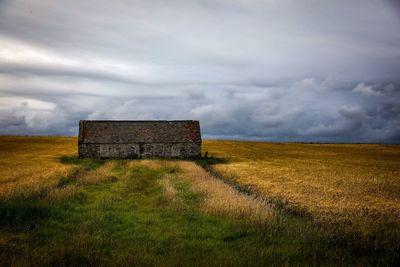 Abandoned house on field against storm clouds