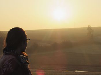 Silhouette teenage girl looking at bright sun during sunset