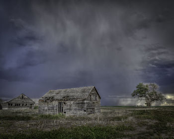 Abandoned house on field against storm clouds