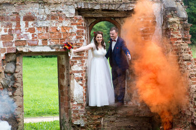 Full length of newlywed couple standing by abandoned built structure