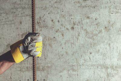 Cropped hand of worker holding metallic rod against concrete wall