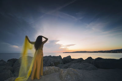 Woman in a yellow dress and cape observing a magnificent sunrise on the french basque coast i