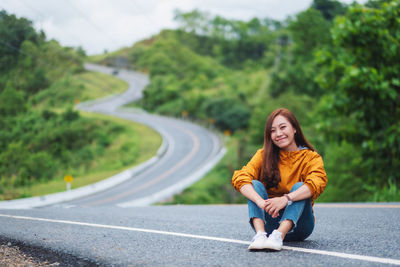 Portrait image of a beautiful young asian female traveler sitting on the street in countryside