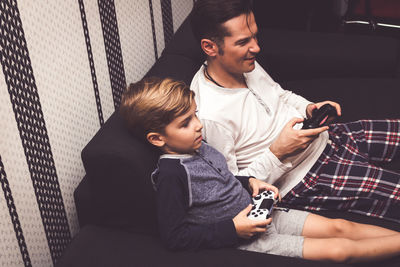 Father and son playing video games while sitting on sofa