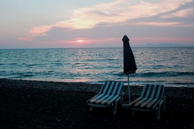 Chair on beach against sky during sunset