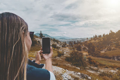 Girl is shooting of beautiful sundown on smartphone, while is standing against scenery background