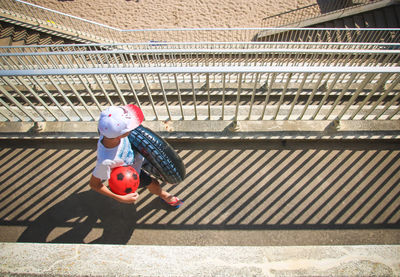 High angle view of boy with ball and tire walking on footbridge