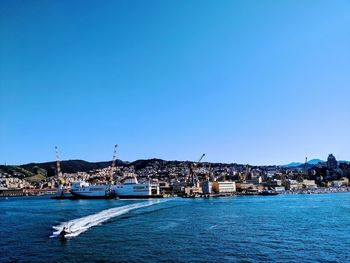 Sailboats in sea by buildings against clear blue sky