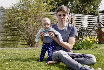 Portrait of young man with baby sitting on grass in yard