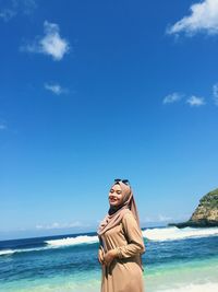 Portrait of young woman on beach against blue sky