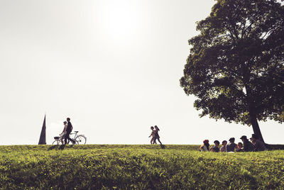 People on grassy field against clear sky