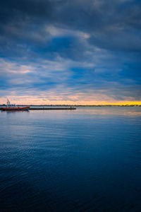 Sunset on the sea with cloudy sky and small harbor with dinghy and people