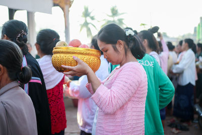 Woman holding apples in container while standing with crowd in city