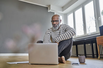 Mature man sitting on floor, working on laptop