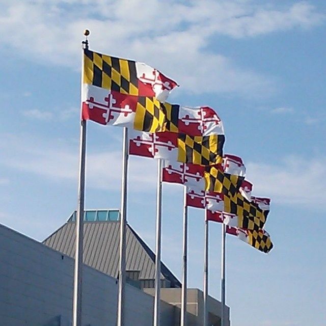 low angle view, sky, built structure, architecture, flag, building exterior, national flag, identity, patriotism, multi colored, text, cloud, cloud - sky, day, american flag, blue, western script, no people, outdoors, communication