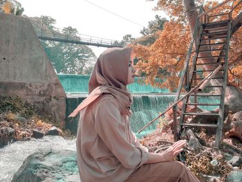 Side view of young woman looking away while sitting on rock