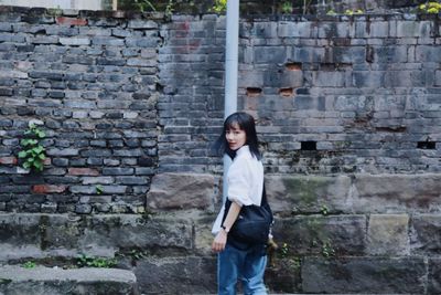 Full length of woman standing against brick wall