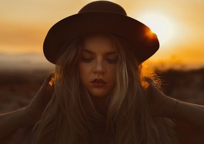 Close-up of young woman wearing warm clothing while standing against sun during sunset
