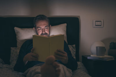 Man in pajamas reading a book lying on bed at late at night. boy sitting in bedroom reads at home. 