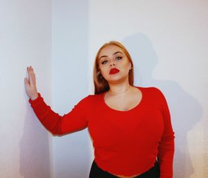 Portrait of young woman wearing red top standing against wall