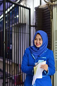 Portrait of smiling woman wearing hijab while holding documents