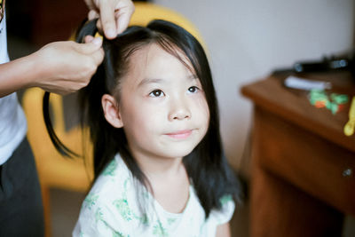 Cropped image of woman braiding daughter hair at home