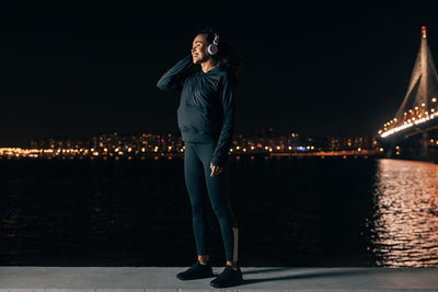 Full length of woman standing by illuminated city at night