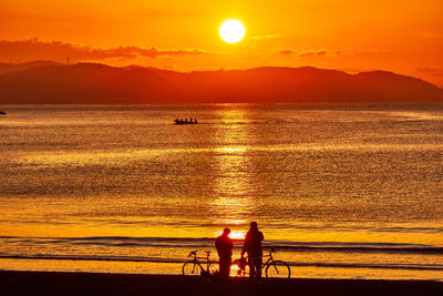 Scenic view of sea with silhouette people against orange sky during sunrise