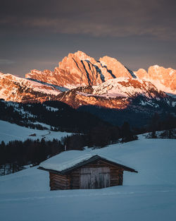 Hut on snow covered landscape against sky