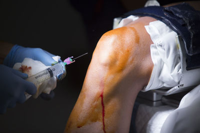 Cropped hands of doctor holding syringe by patient knee in operating room