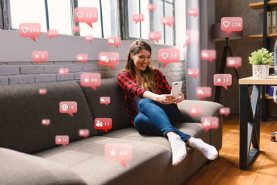 Happy young woman using phone while sitting on laptop