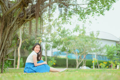 Portrait of woman sitting on grass against trees