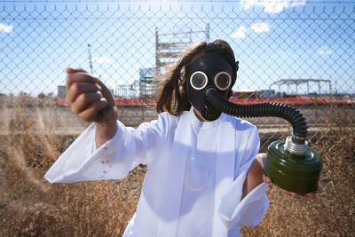 Portrait of girl wearing gas mask while standing by fence