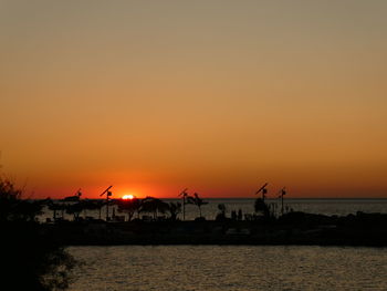 Silhouette buildings by sea against orange sky