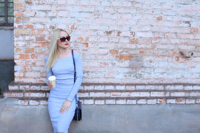 Young woman standing against brick wall