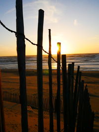 Wooden fence at beach against sky during sunset