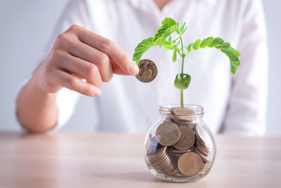 Midsection of woman putting coin in jar on table