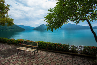 Empty bench by swimming pool against sky