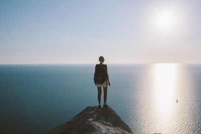 Rear view of young woman standing at sea shore against clear sky